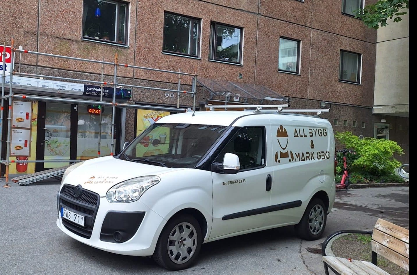 All Bygg & Marks firmabil parkerad framför en närbutik i Göteborg med byggställning uppe längs fasaden